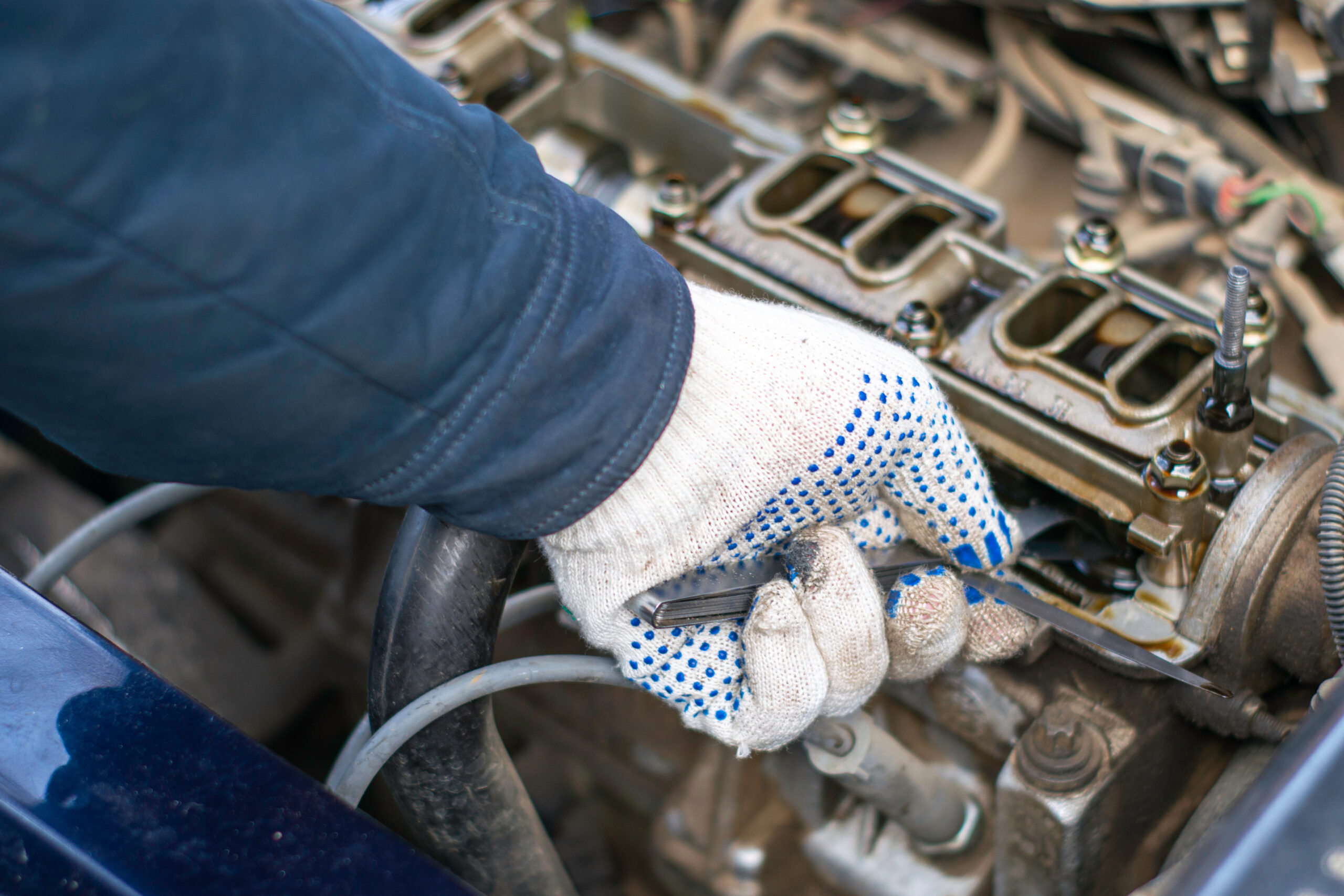 the mechanic adjusts the gap in the valve mechanism of the car engine with the help of dipsticks Automaster top up the oil in a car engine.